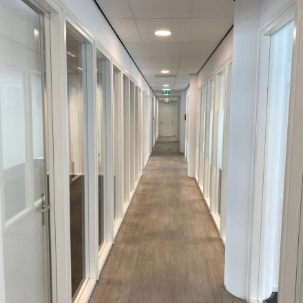 A long hallway with glass doors on both sides in an office building at Regulusweg 11, Voorburg. Natural light illuminates the hallway, suggesting potential office space rentals for private offices.