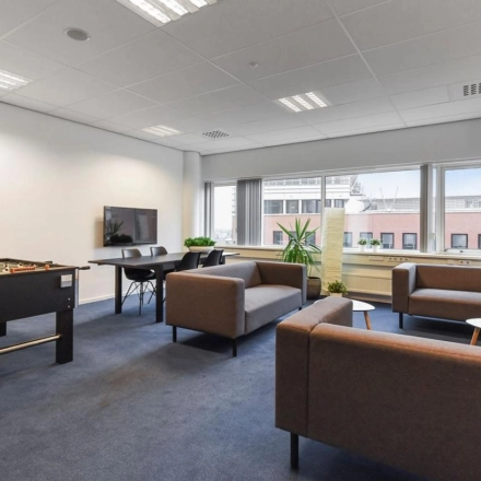 Modern furnished office space for rent at Regulusweg 11, Voorburg, featuring a foosball table, seating area, and large windows.