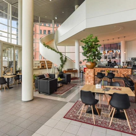 Spacious office lounge at Regulusweg 11, Voorburg featuring modern furniture for rent office space with a relaxed seating area and coffee bar. Numerous plants enhance the inviting atmosphere.