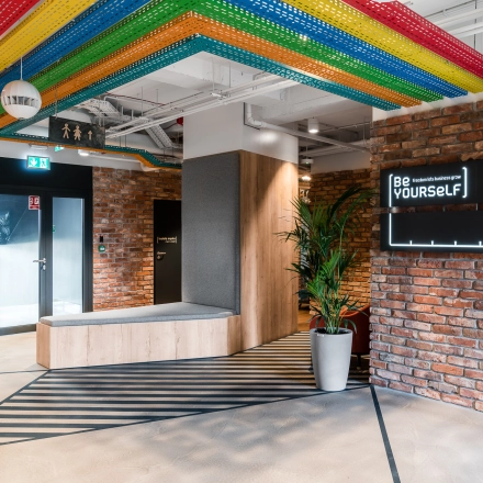 Stylish office space at Konstruktorska 11, Warsaw Mokotow, featuring exposed brick walls and colorful ceiling accents, available for rent.