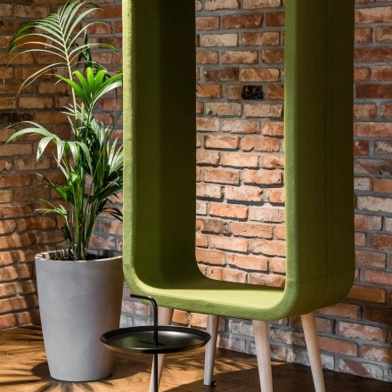 Cozy corner at the office space rental in Konstruktorska 11, Warsaw Mokotow, showcasing a modern green acoustic pod and a sleek black side table.
