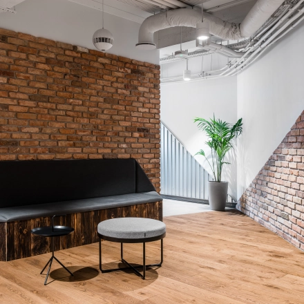 Cozy lounge area with brick walls at an office space rental on Konstruktorska 11, Warsaw Mokotow, featuring modern seating and a small table.