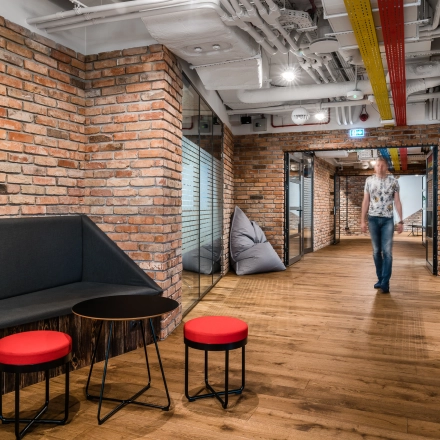 Modern office interior at Konstruktorska 11, Warsaw Mokotow, featuring brick walls, seating area, and a person walking, ideal for office space rental.
