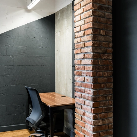 A cozy office space with a brick column, wooden flooring, and a desk with an office chair, ideal for office space rental in Warsaw Mokotow.