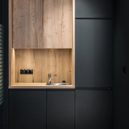 Modern office kitchen area with sleek black cabinets and wooden accents at Konstruktorska 11, Warsaw Mokotow. Ideal for office space rental.