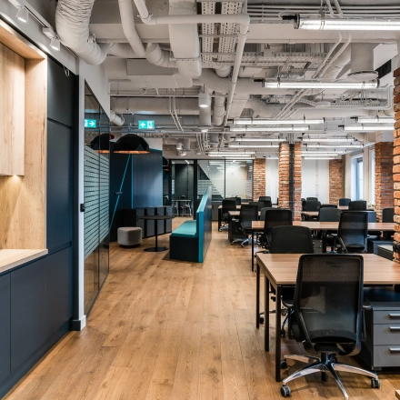 Modern office space with wooden floors, brick accent columns, and a mix of wood and metal furnishings at Konstruktorska 11, Warsaw Mokotow. Perfect for those looking for office space rental.