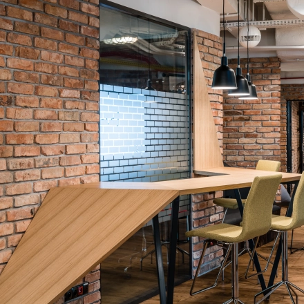 Modern workspace with high stools and wooden table in an office to rent, showcasing brick walls and contemporary lighting in Warsaw Mokotow.