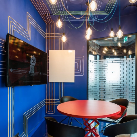 Unique and colorful meeting area with vibrant blue walls and exposed light bulbs, ideal for office space rental at Konstruktorska 11, Warsaw Mokotow.