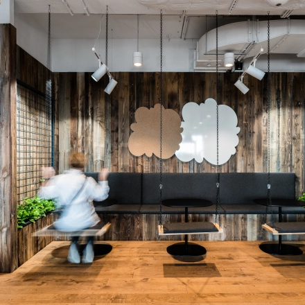 Modern office space with wooden walls at Konstruktorska 11, Warsaw Mokotow, featuring unique seating designs and plants, ideal for rent office space. A person is adjusting seating arrangements.