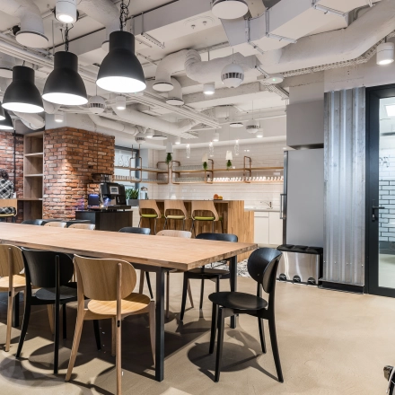 Modern office space at Konstruktorska 11, Warsaw Mokotow with a large wooden table, chairs, and a kitchenette area, ideal for office space rental.