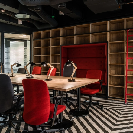 Furnished office space for rent at Konstruktorska 11, Warsaw Mokotow, featuring a stylish open floorplan with red chairs and industrial shelving.
