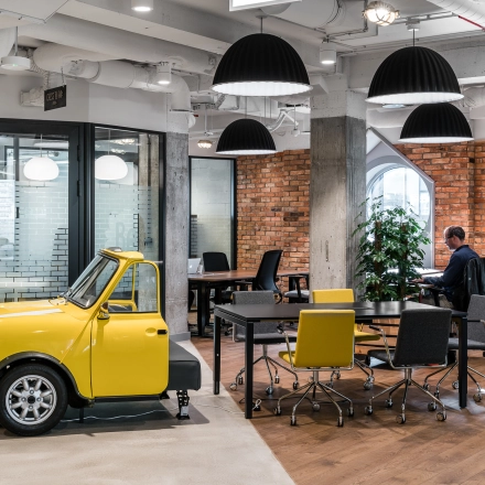 Office space rental at Konstruktorska 11, Warsaw Mokotow featuring a unique yellow car sculpture, modern workstations, and a person working at a desk.