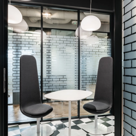 Modern office space to rent at Konstruktorska 11, Warsaw Mokotow, featuring sleek black and white decor with high-backed chairs and a round table.