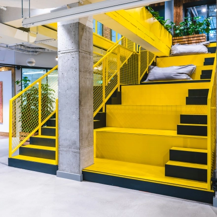 Modern office interior at Konstruktorska 11 in Warsaw Mokotow featuring vibrant yellow staircases and industrial design, ideal for office space rental.