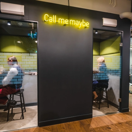 Two individuals work in private phone booths with glass doors in a modern office located at Konstruktorska 11, Warsaw Mokotow. Ideal office space rental for focused calls.