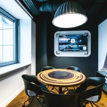 Modern furnished conference room at Konstruktorska 11, Warsaw Mokotow, featuring a round table, chairs, a wall-mounted screen, and a flip chart. Ideal office space rental for meetings.