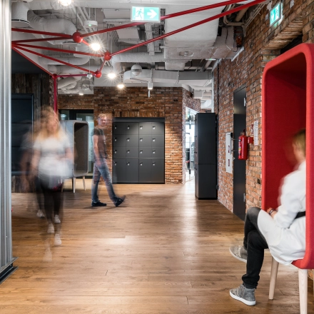 Modern office interior at Konstruktorska 11, Warsaw Mokotow, featuring stylish seating and employees engaging in business activities. Ideal office space rental for dynamic work environments.