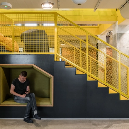Modern office space at Konstruktorska 11, Warsaw Mokotow, featuring a vibrant yellow stair design with a cozy seating nook where a person is working on a laptop.