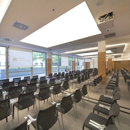 Spacious conference room with rows of black chairs, large windows, and modern lighting at Postępu 17A, Warsaw Mokotow for office space rental.