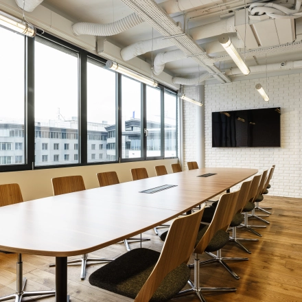 Spacious conference room in Warsaw Ochota with a long wooden table, modern chairs, and a large screen, ideal for office space rental meetings.
