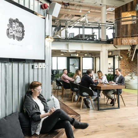 Modern office space with people engaged in discussions around tables at Al. Jerozolimskie 181B, Warsaw Ochota. Ideal for those looking to rent office space with a collaborative atmosphere.