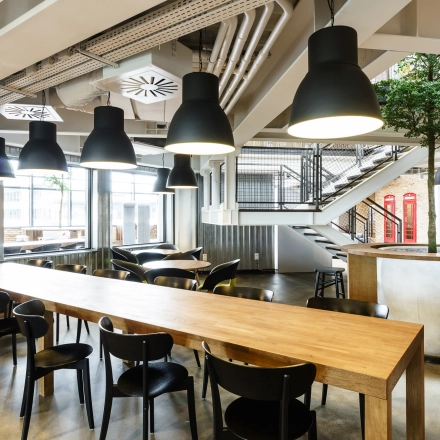 Spacious modern workspace with rows of tables and chairs under stylish lighting, suitable for office space rental in Warsaw Ochota at Al. Jerozolimskie 181B.