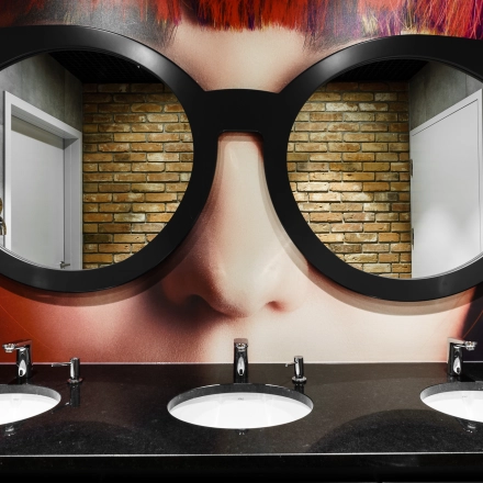 Stylish bathroom with artistic decor, mirrors shaped like large eyeglasses above three sinks. Located at Al. Jerozolimskie 181B, Warsaw Ochota, a unique office space rental opportunity.