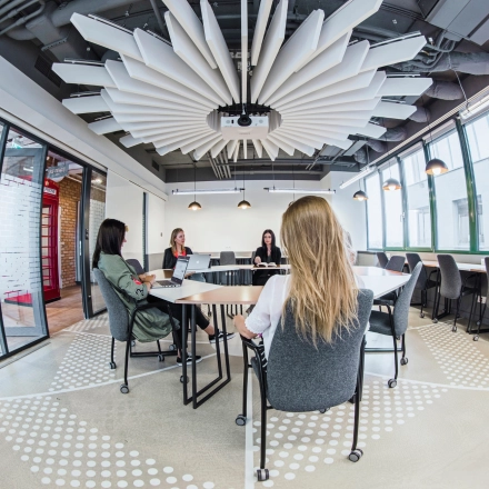 Modern office space in Warsaw Ochota at Al. Jerozolimskie 181B featuring a conference area with tables where people are engaged in business discussions, ideal for office space rental.