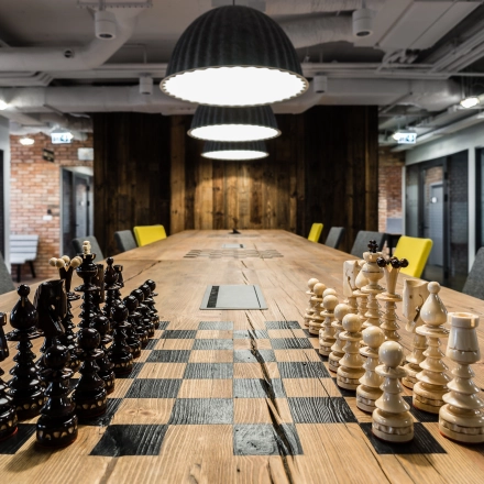 A modern workspace in Warsaw Ochota features a long table with chess sets, ideal for office space rental.