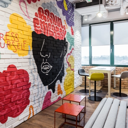 A creatively designed office space in Warsaw Ochota with vibrant graffiti art on the walls, cozy seating, and a view from the window. Ideal for office space rental.