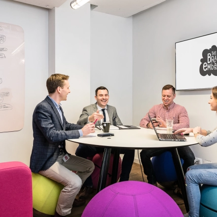 Office space for rent at Al. Jerozolimskie 181B, Warsaw Ochota, featuring a lively meeting area with professionals brainstorming and collaborating around a round table.