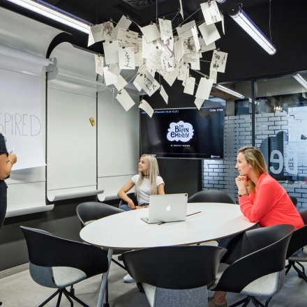 Three people in a modern office to rent at Al. Jerozolimskie 181B in Warsaw Ochota, collaborating around a table with a large screen and whiteboard.