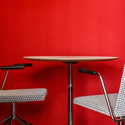 Furnished office space with two modern chairs and a small round table against a vibrant red wall, ideal for quick meetings or discussions.