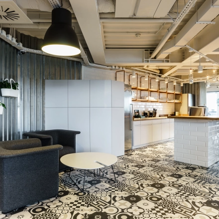 Modern office space for rent in Warsaw Ochota, featuring a stylish lounge area with seating and a coffee bar under industrial lighting.