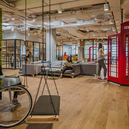 Vibrant and modern office space for rent with unique decor, including red phone booths and flexible seating areas, at Al. Jerozolimskie 181B, Warsaw Ochota. People engage in various business activities.