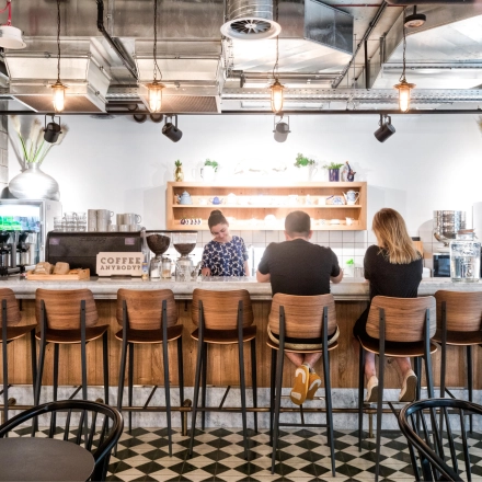 A modern office lounge at Koszykowa 61, Warsaw Śródmieście, featuring a bar counter with three people engaged in conversation, ideal for casual meetings and office space rental.