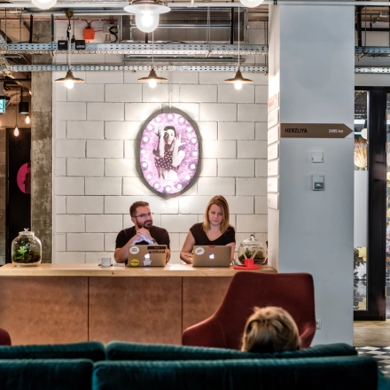 A modern, furnished office space in Warsaw Śródmieście with two people working on laptops at a reception desk, highlighting an inviting office space rental option.