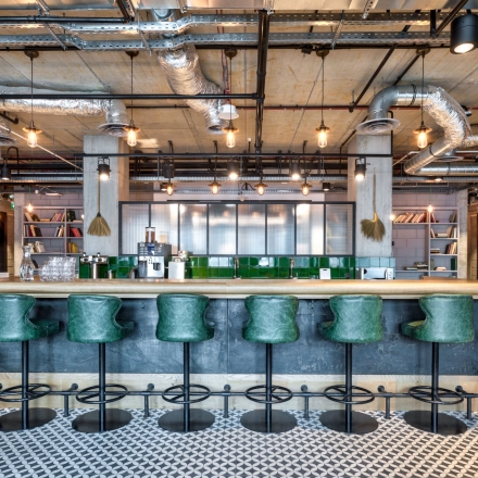 Modern office space at Koszykowa 61 in Warsaw Śródmieście featuring a chic bar area with green stools and industrial design elements, ideal for office space rental.