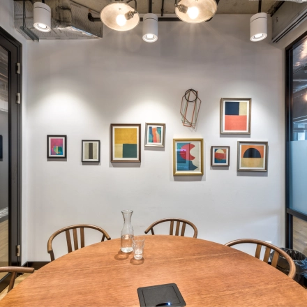 Furnished meeting room with a round wooden table and artistic wall decor, perfect for those looking to rent office space in Warsaw Śródmieście.