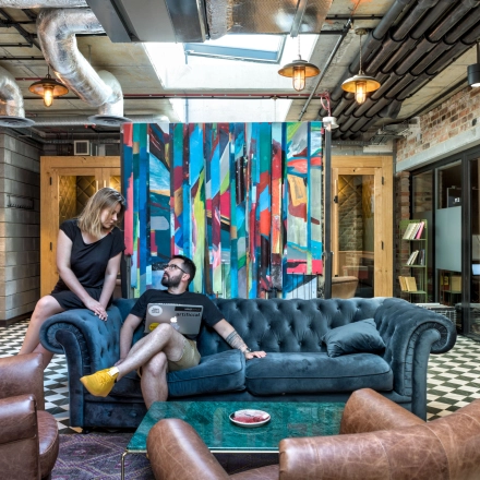 A vibrant office space with colorful decor at Koszykowa 61, Warsaw Śródmieście. Two people engage in discussion on a plush sofa. Ideal for rent office space with creative ambiance.