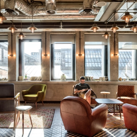 Cozy office lounge at Koszykowa 61 in Warsaw Śródmieście, ideal for renting office space, featuring eclectic seating and industrial lighting.