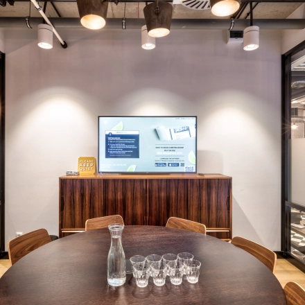 Furnished conference room at Koszykowa 65 in Warsaw Śródmieście, ideal for office space rental, featuring a round table and a presentation screen.