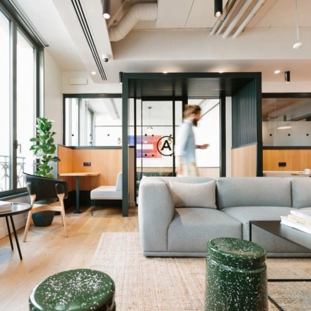 A modern office space with stylish seating at Krakowskie Przedmieście 13, Warsaw. People are working, utilizing the office space rental with sleek furniture and ample natural light.
