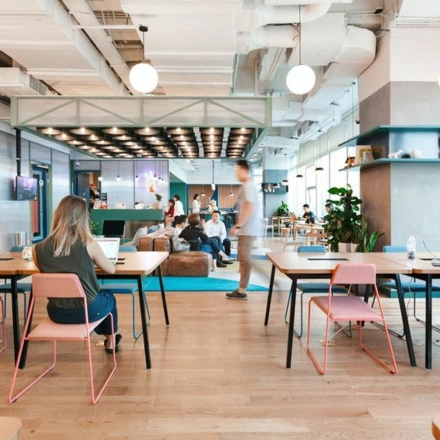 Modern office space rental at Krakowskie Przedmieście 13, Warsaw Śródmieście, featuring furnished open workspaces with people working on laptops, vibrant lighting, and a lounge area in the background.