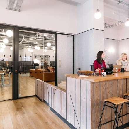 Inside an office space rental at Krakowskie Przedmieście 13, Warsaw Śródmieście, featuring a reception area with wooden seating and three people discussing work.