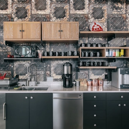 A modern kitchenette in an office space with coffee machines, shelves, and a stainless steel sink, ideal for office space rental in Warsaw Śródmieście.
