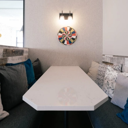 Cozy office space with a long table surrounded by cushioned seating and modern decor, ideal for casual meetings or breaks. Perfect for those seeking office space rental in the heart of Warsaw Śródmieście.
