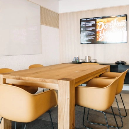 Furnished office space at Krakowskie Przedmieście 13 in Warsaw Śródmieście, featuring a wooden table and yellow chairs under a wall-mounted screen, ideal for office space rental.