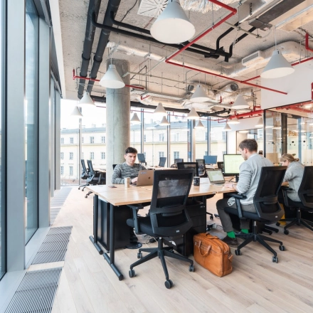 Modern workspace at Krucza 50, Warsaw Śródmieście, featuring large windows and professionals engaged in business activities. Ideal office space rental opportunity with sleek interiors.