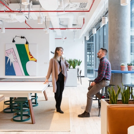 Office space at Krucza 50 in Warsaw Śródmieście with modern decor and plants. Two people discuss business near a table.